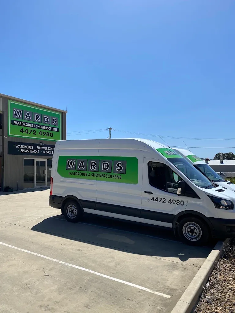 A white Wards Wardrobes & Showerscreens van parked in front of the Wards workshop on Cranbrook Road, Batemans Bay, with a second van behind it and the green Wards sign on the building.