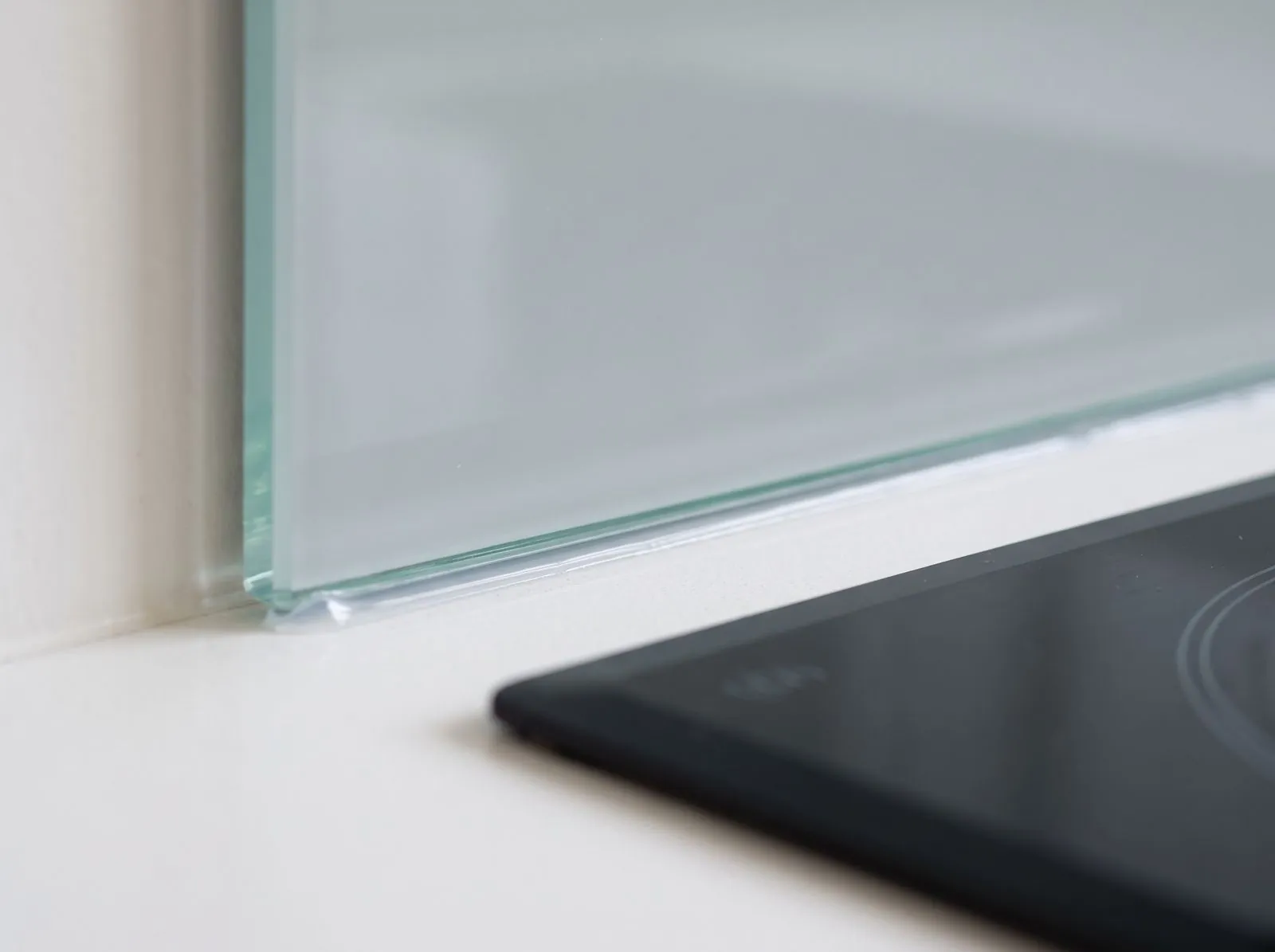Close-up of a glass splashback edge meeting a dark benchtop