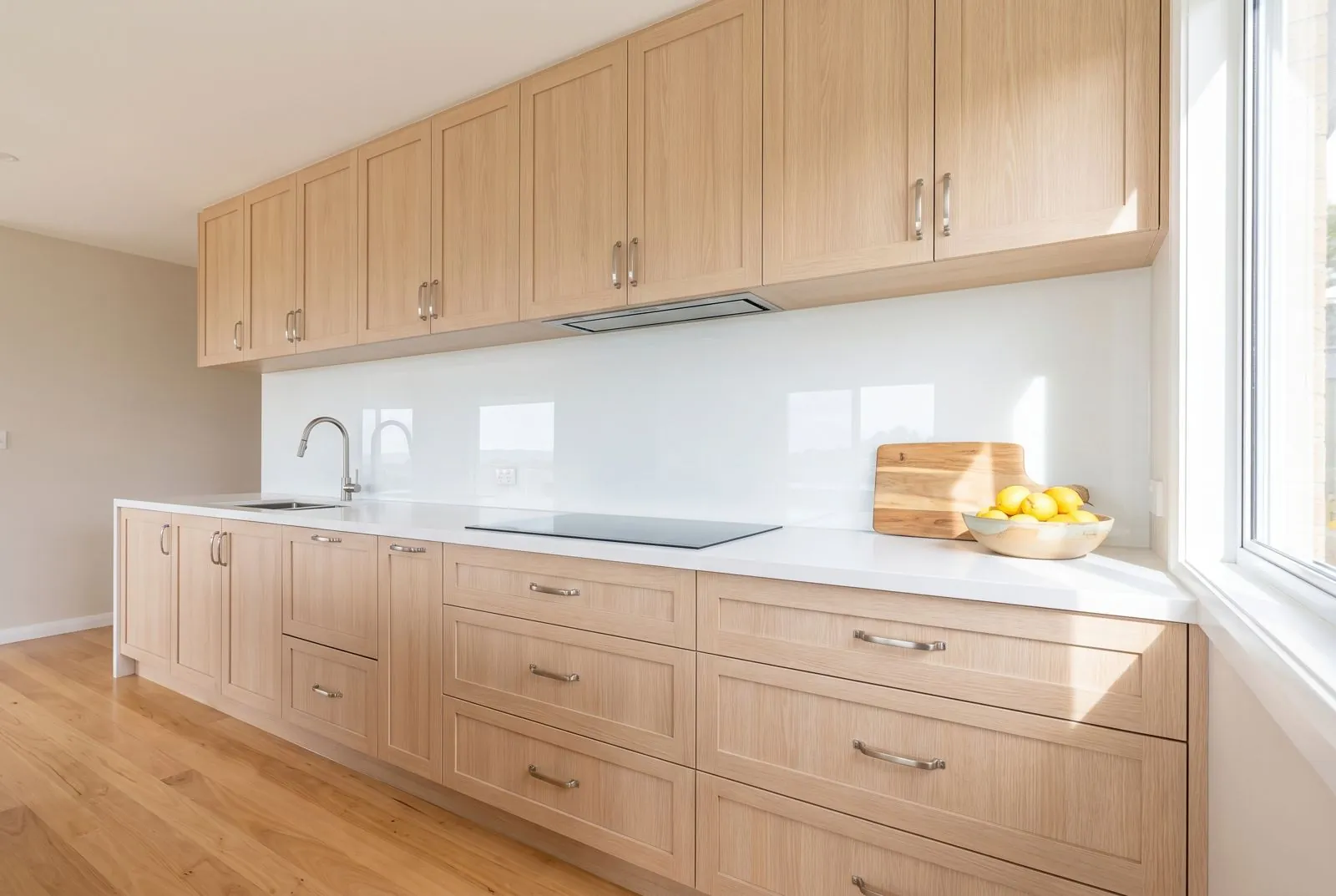 Pale timber kitchen with a white glass splashback