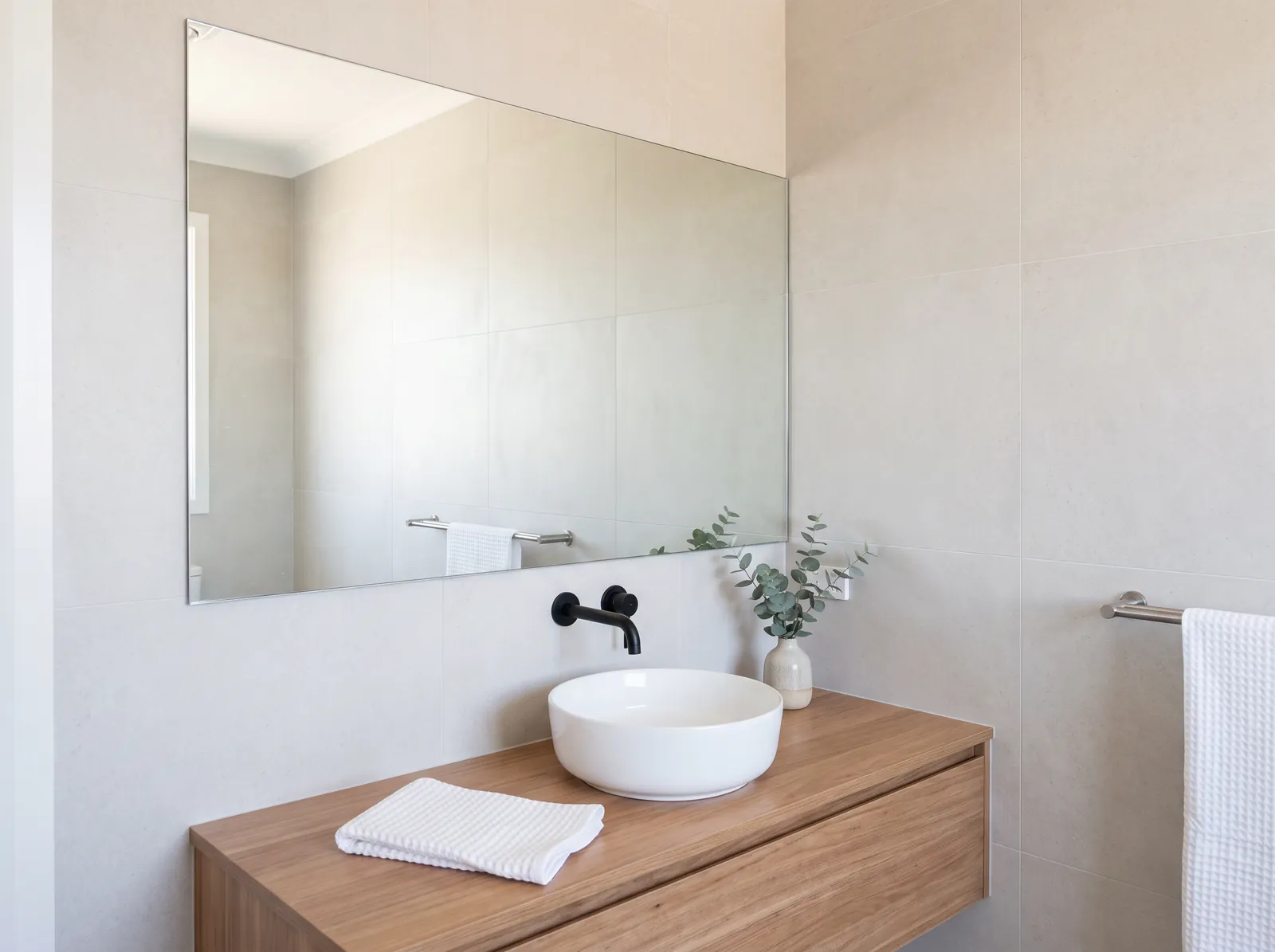 Frameless bathroom mirror above a timber vanity with a white basin